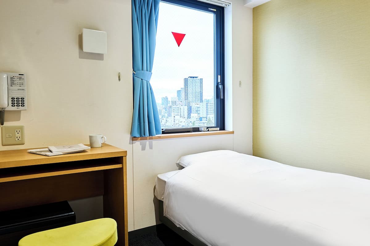 A hotel room with a bed, a desk with a telephone, a chair, and a window with a city view.