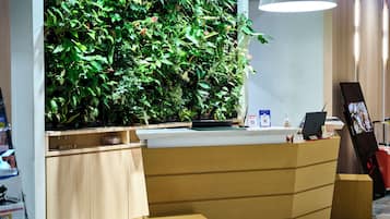 A reception desk with a vertical garden, wooden cabinets, a laptop, and a digital display.