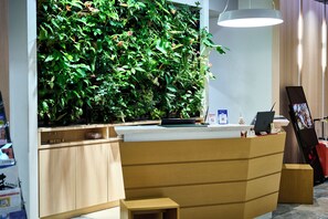 A reception desk with a vertical garden, wooden cabinets, a laptop, and a digital display.