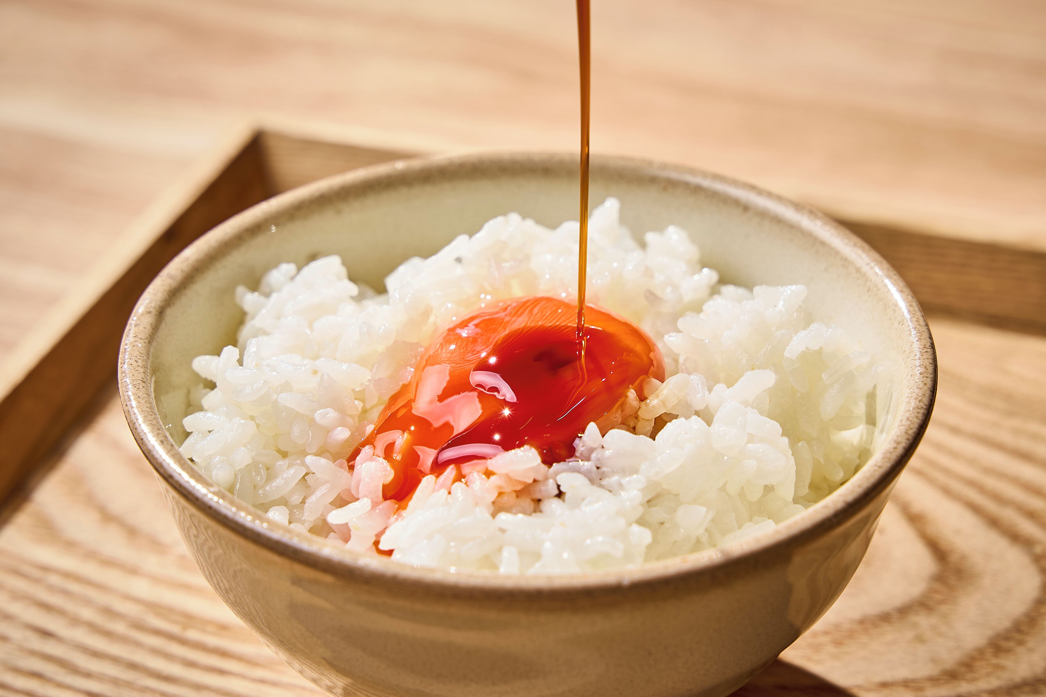 A bowl of white rice with a red sauce being poured over it.