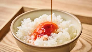 A bowl of white rice with a red sauce being poured over it.