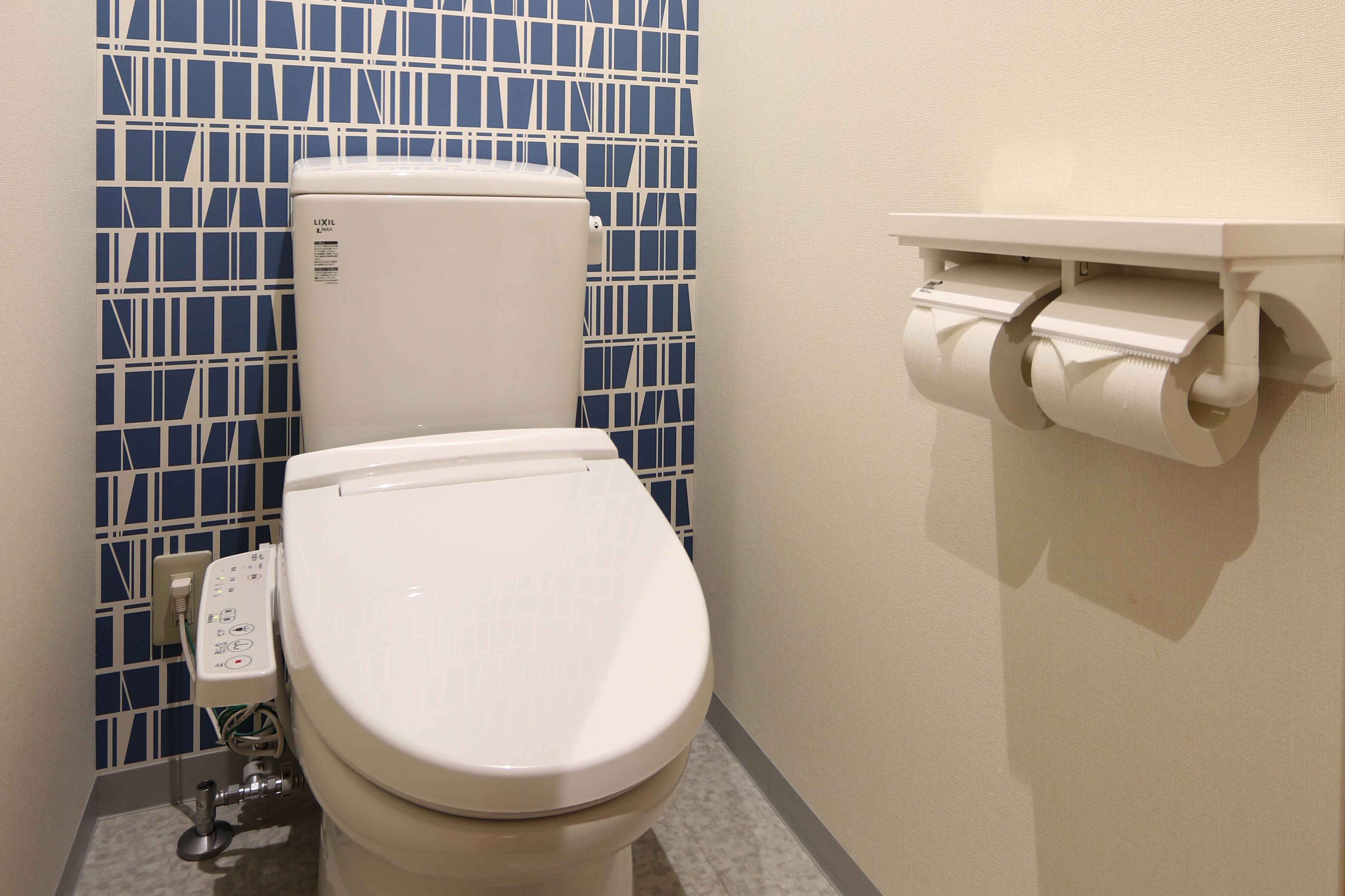 Un inodoro con un panel de control, un rollo de papel higiénico y una pared de azulejos azules.