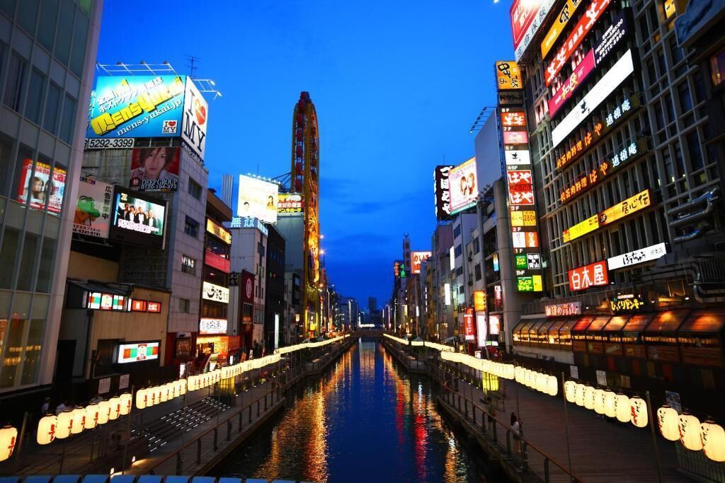 A nighttime view of a city street with illuminated buildings and a canal in the center.