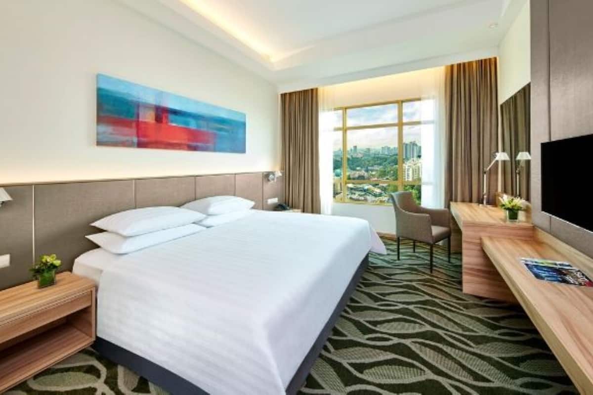 Une chambre d’hôtel avec un grand lit, un bureau avec une télévision, une chaise et une fenêtre donnant sur la ville.