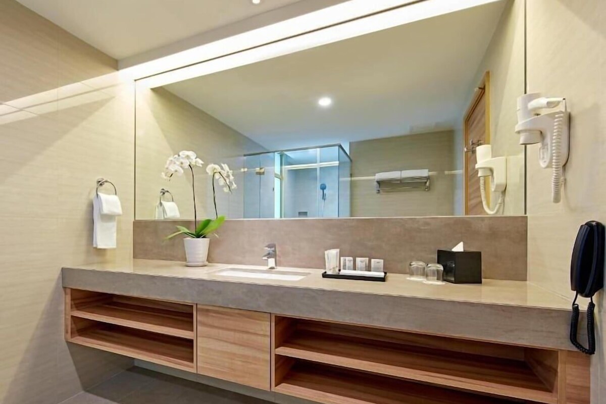 A modern bathroom with a large mirror, a sink, a potted orchid, and a telephone.