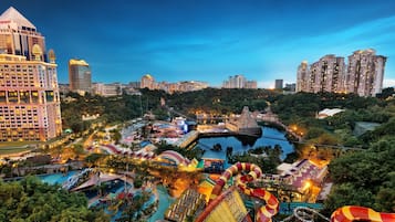 Un hotel grande con varios edificios altos al fondo, un parque acuático con diversas toboganes y piscinas, y un puente sobre el agua.