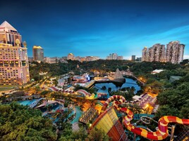 Un grand hôtel composé de plusieurs immeubles de grande hauteur, un parc aquatique avec différents toboggans et piscines, et un pont enjambant une étendue d’eau.