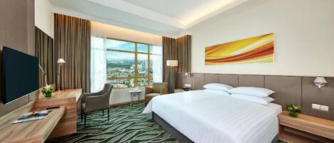 A hotel room with a large bed, a desk with a chair, a TV, and a view of the city.
