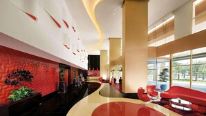 A modern hotel lobby with a curved reception desk, red seating, and a large window offering a view of palm trees. - Sunway Lagoon Hotel (formerly Sunway Clio Hotel) (Petaling Jaya)
