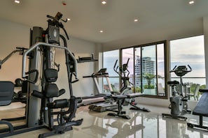 Une salle de sport moderne dotée de divers équipements d’exercice, de grandes fenêtres offrant une vue sur la ville, et d’un aménagement propre et spacieux.