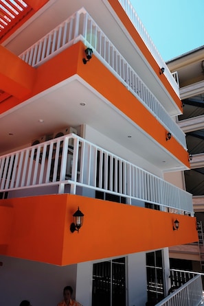 A multi-story building with orange and white exterior walls, balconies with white railings, and black wall-mounted lights. - Sunset Apartments (Pattaya)