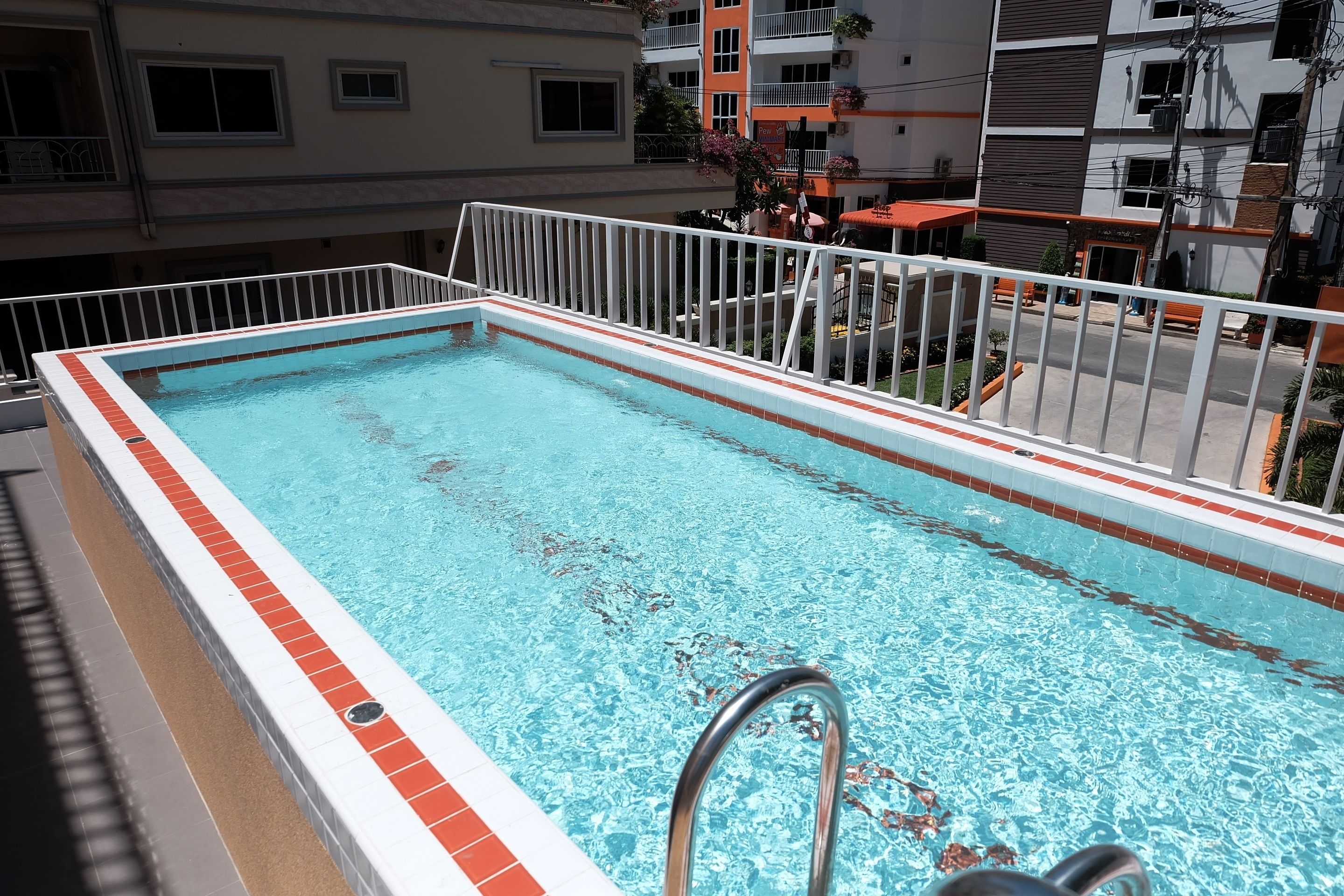 Ein rechteckiger Swimmingpool mit weiß-roten Fliesen und einer weißen Metallumrandung.