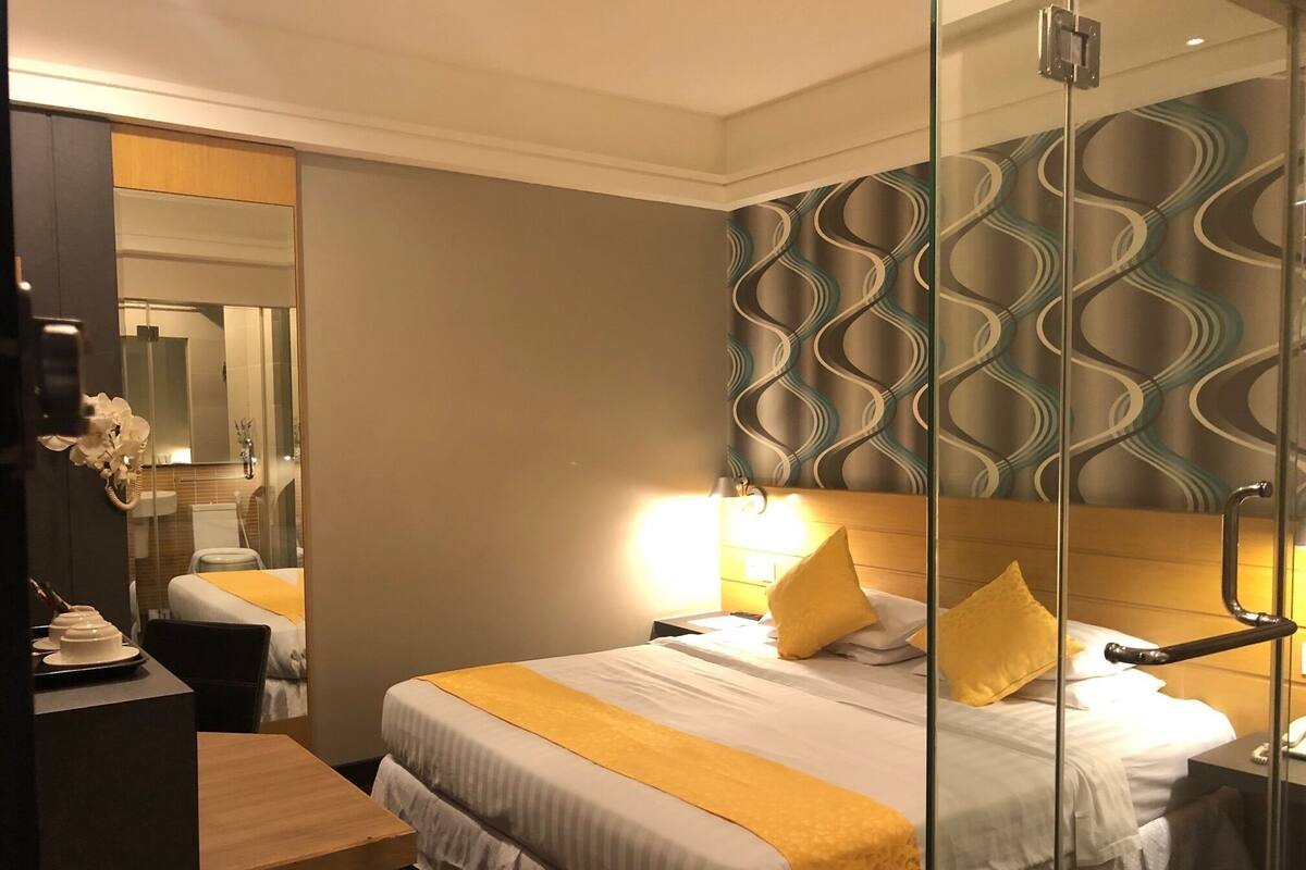 A hotel room with a bed, bedside table, and a mirror.