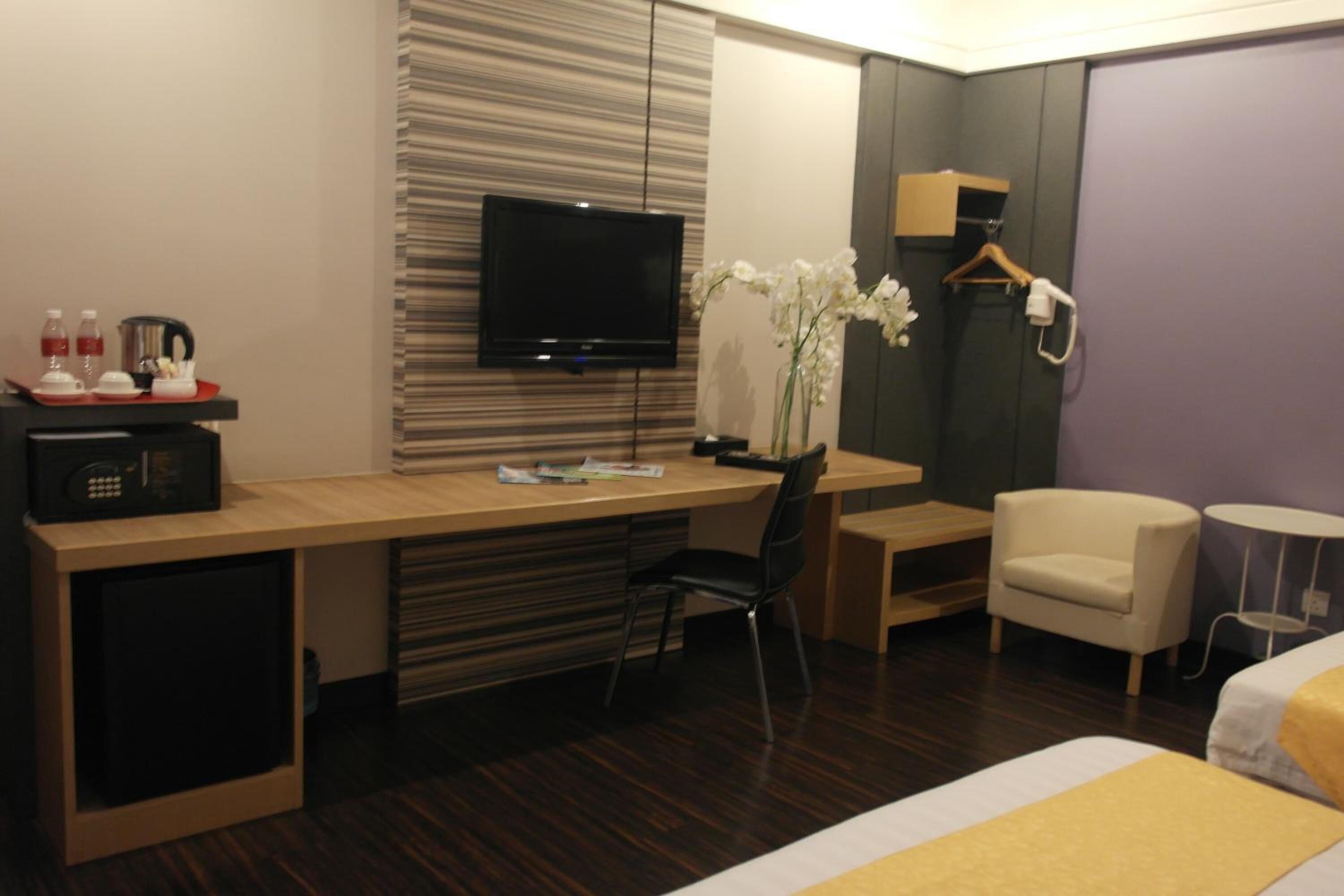 Ein Hotelzimmer mit Holzschreibtisch, Fernseher, Stuhl, Bett und einem kleinen Tisch mit Blumen in einer Vase.