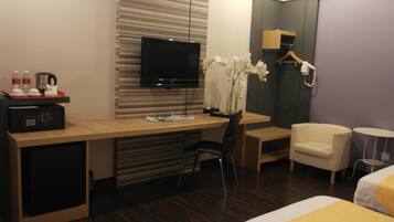 Ein Hotelzimmer mit Holzschreibtisch, Fernseher, Stuhl, Bett und einem kleinen Tisch mit Blumen in einer Vase.
