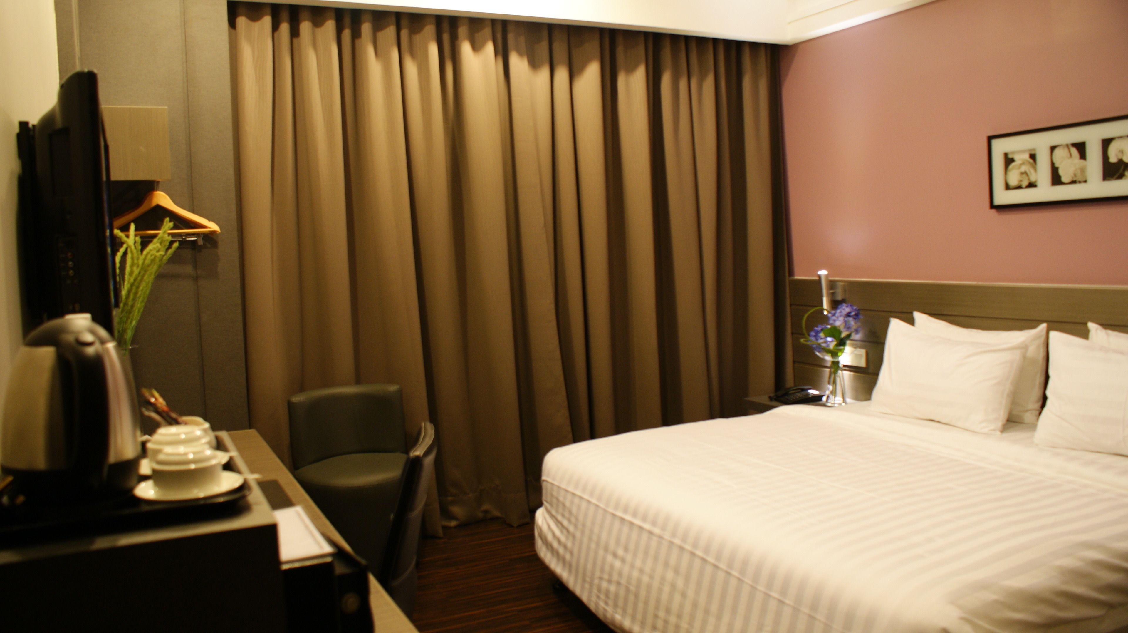 Hotelkamer met een bed, een bureau met telefoon, een stoel en een nachtkastje met een bloemetje.
