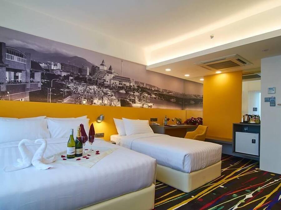 A hotel room with two beds, a mural of a cityscape, a minibar, and a desk with a chair.