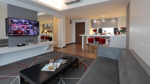 Un salon moderne doté d’un téléviseur à écran plat, d’un canapé, d’une table basse et d’un coin cuisine avec des tabourets de bar rouges.