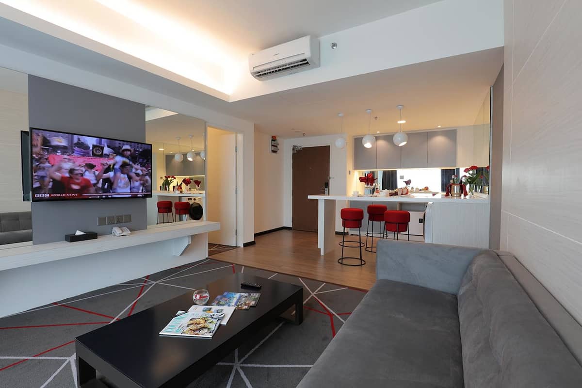 Una sala de estar moderna con un televisor de pantalla plana, un sofá, una mesa de centro y una zona de cocina con taburetes rojos.