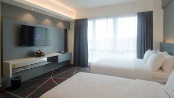 A hotel room with two beds, a TV on the wall, a small table with a vase of flowers, and a large window with curtains.