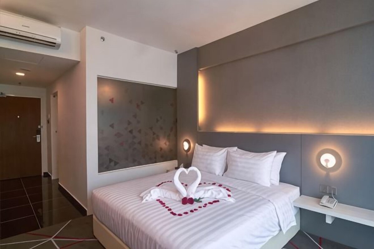 Una habitación de hotel con una cama grande, una mesita de noche, una lámpara de pared y un panel decorativo.