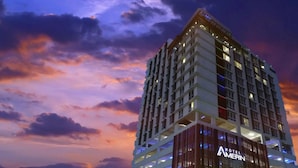 Un hôtel de grande hauteur au design moderne, comprenant de nombreux étages et une entrée imposante avec une enseigne lumineuse.