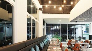 Un restaurant doté d’une longue table à manger, de nombreuses chaises et d’un plafond haut avec des poutres apparentes et des luminaires.