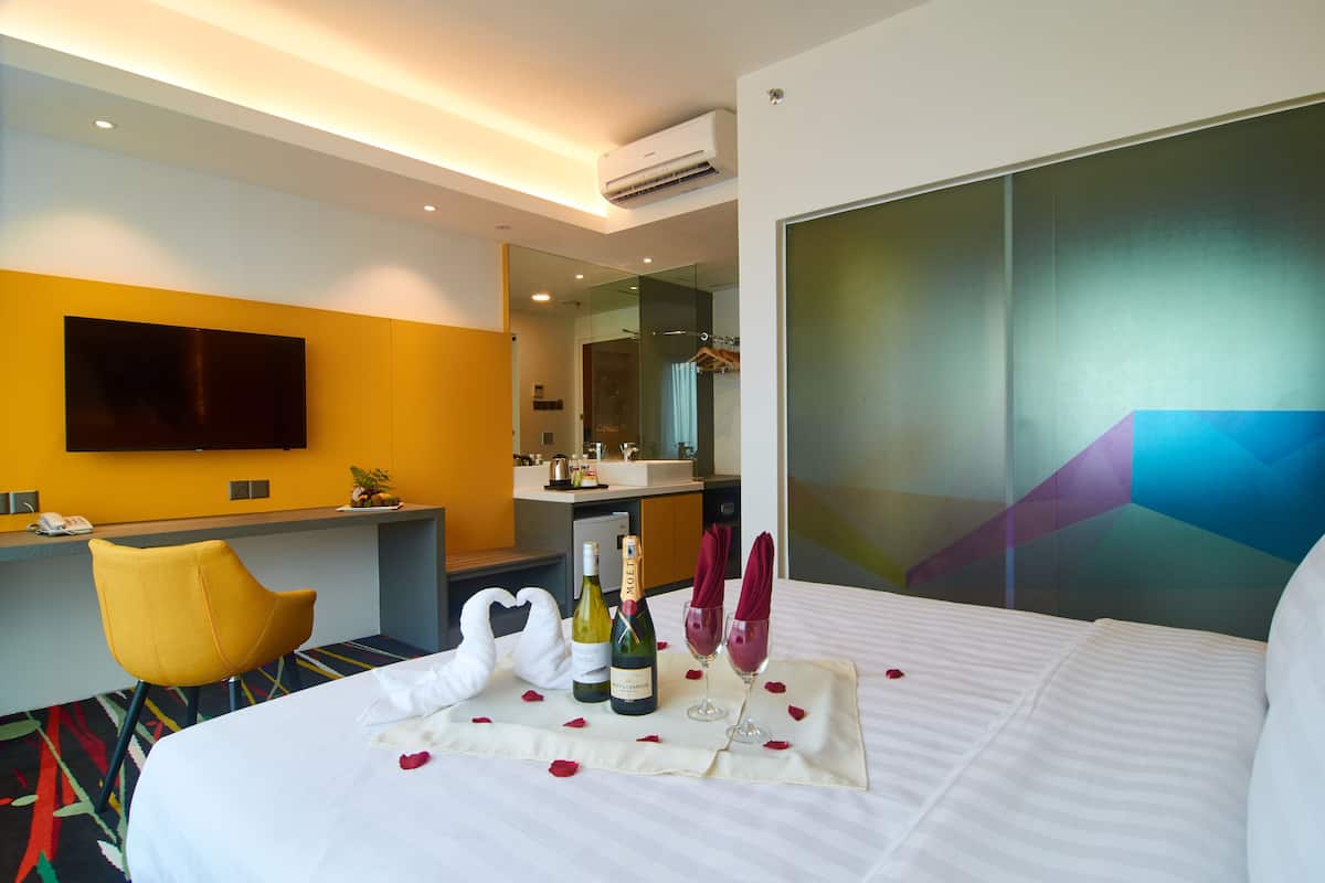 Habitación de hotel con cama, escritorio, silla, minibar y televisión de pantalla plana.