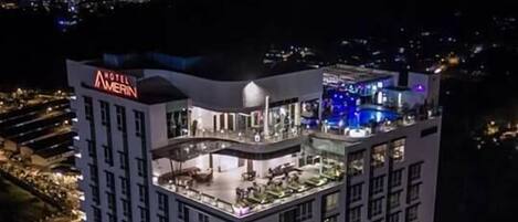 Un hôtel à plusieurs étages doté d’une terrasse sur le toit, d’une enseigne bien visible et d’un espace de stationnement.