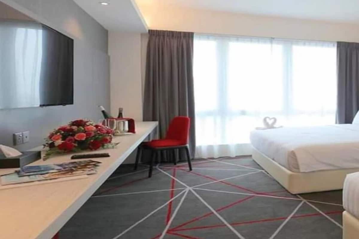 Una habitación de hotel con cama, escritorio con silla, televisor y ventana con cortinas.