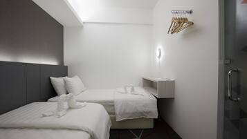 Habitació d'hotel moderna amb dos llits, una petita taula de nit, un suport de tovalloles fixat a la paret i una porta de vidre.