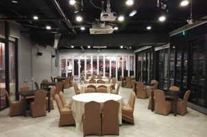 Un salón de conferencias con mesas y sillas redondas, ventanas amplias y un proyector en el techo.