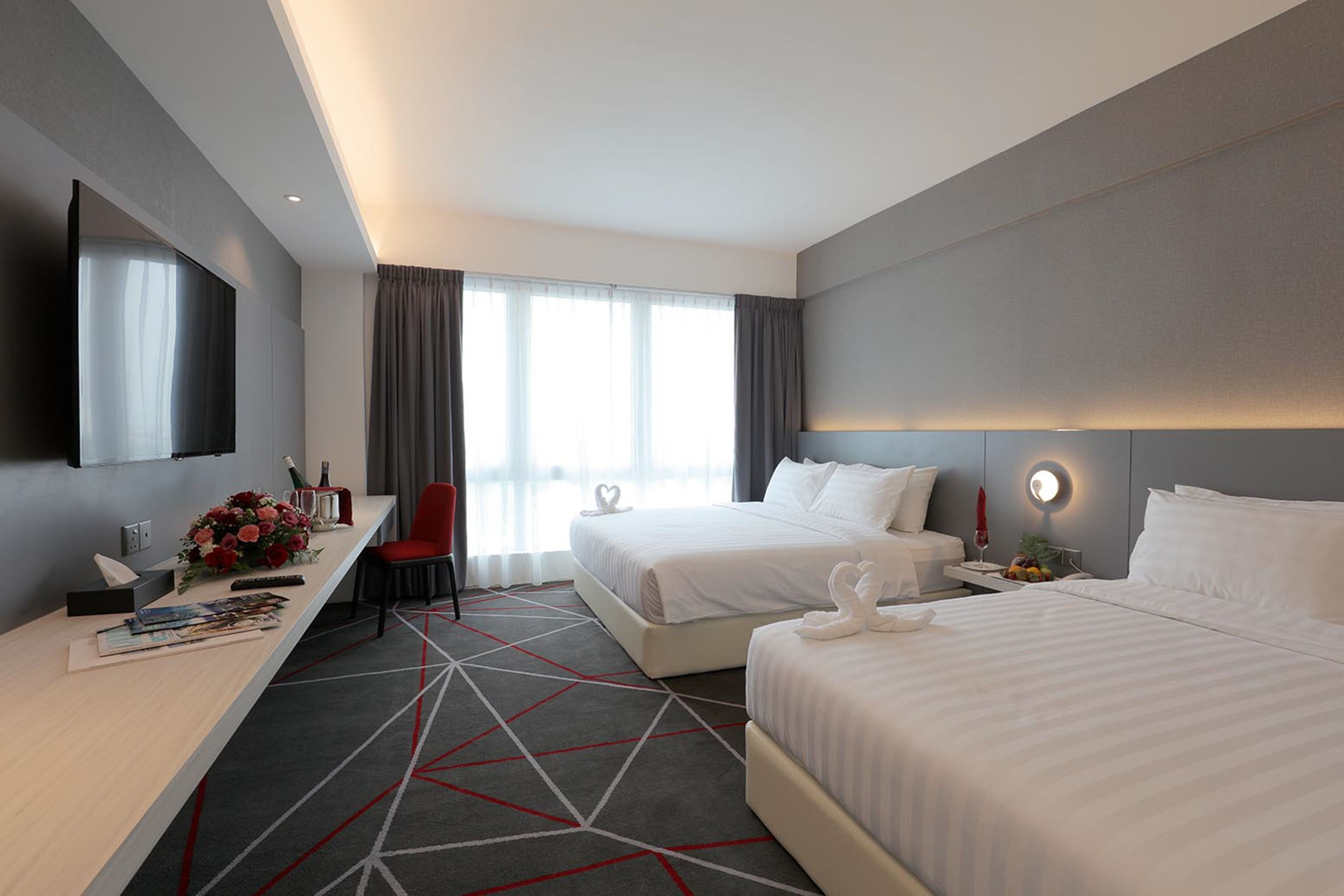 A modern hotel room with two beds, a desk with a computer, a TV, and a large window with curtains.