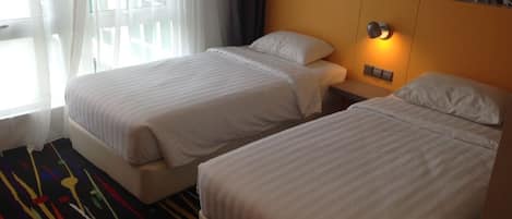 Una habitación de hotel con dos camas individuales, una mesita de noche con lámpara y una alfombra abstracta de colores.