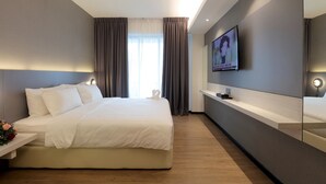 Une chambre d’hôtel moderne avec un grand lit, un téléviseur fixé au mur et une table de chevet avec une lampe.