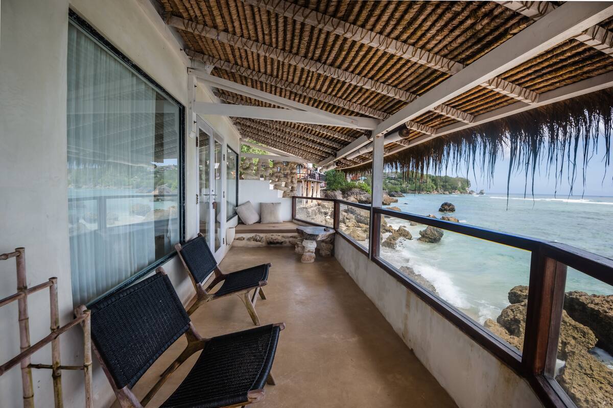A balcony with wicker chairs, a stone table, and a view of the ocean.