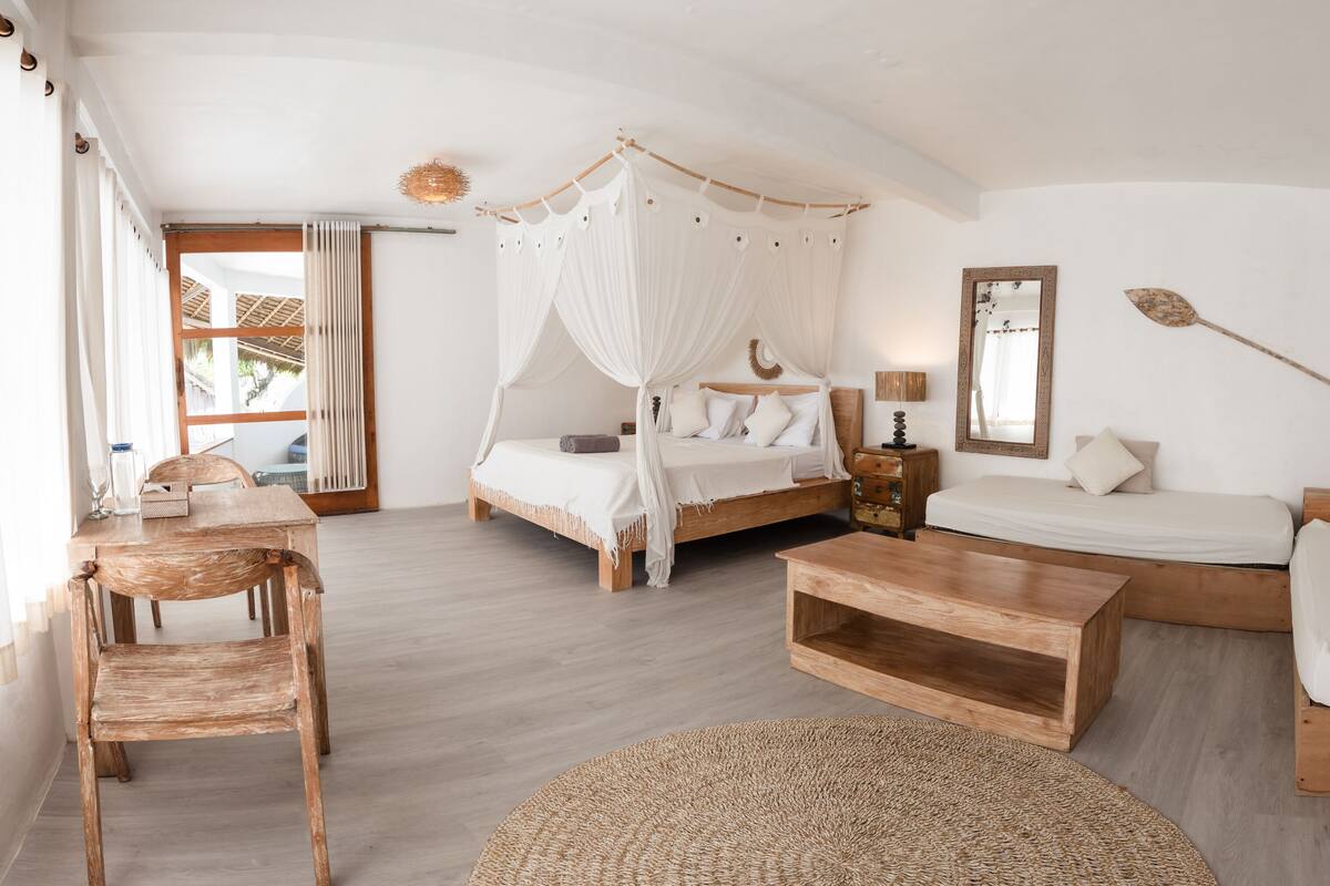 A bedroom with a canopy bed, a sofa bed, a wooden coffee table, and a woven rug.