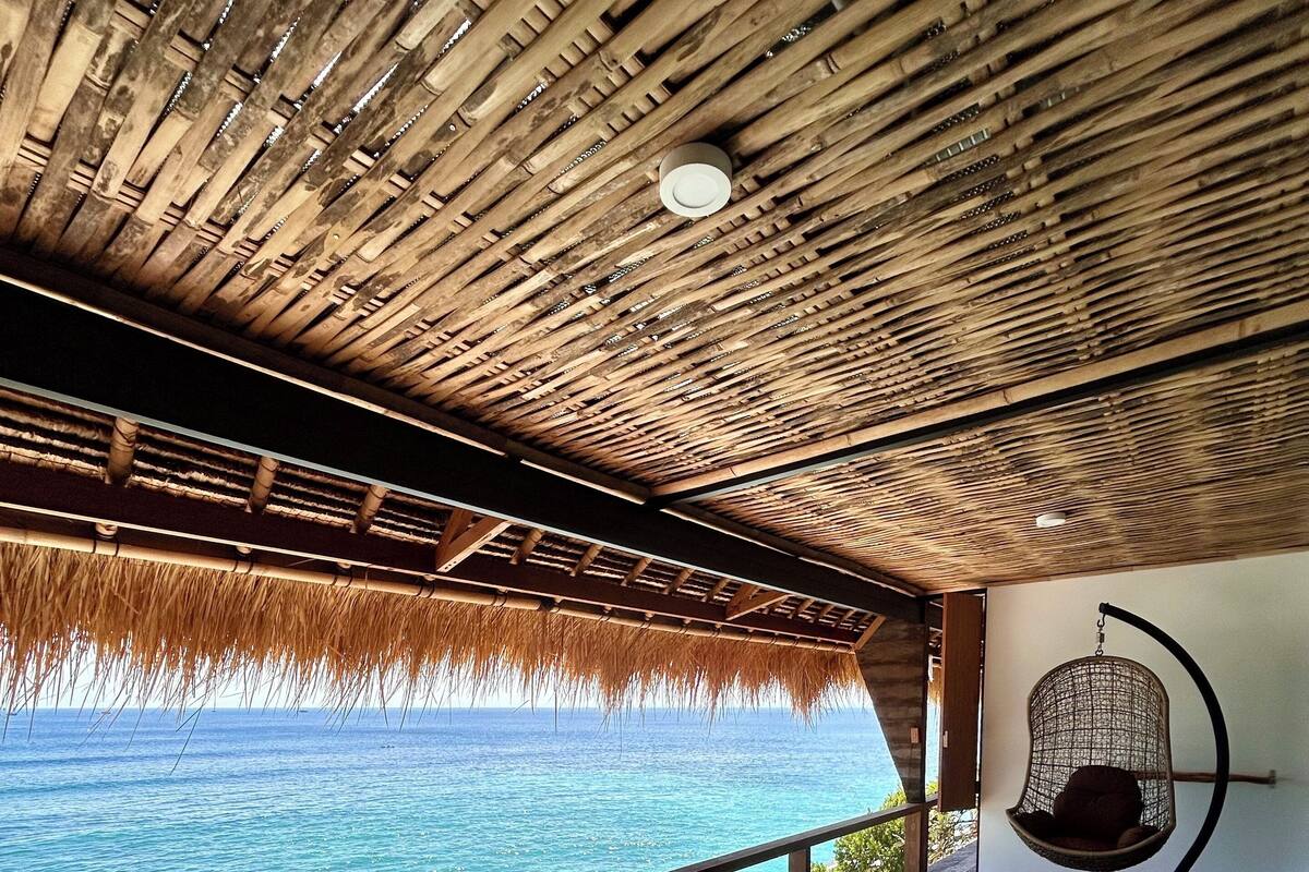 A wooden deck with a thatched roof overlooking turquoise waters.