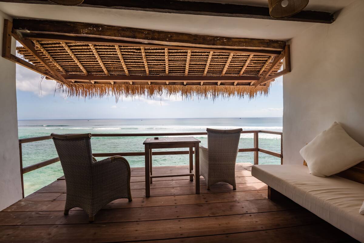 A wooden deck with wicker furniture and a sofa, overlooking a turquoise sea.