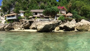 A coastal property with thatched-roof buildings, clear turquoise water, and rocky cliffs. - Rock 'n Reef Hotel (Pecatu)
