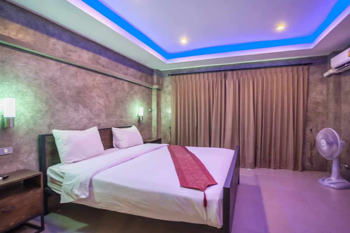 Une chambre d’hôtel équipée d’un lit, d’une table de chevet, d’une lampe fixée au mur, d’un climatiseur et d’un ventilateur de plafond.