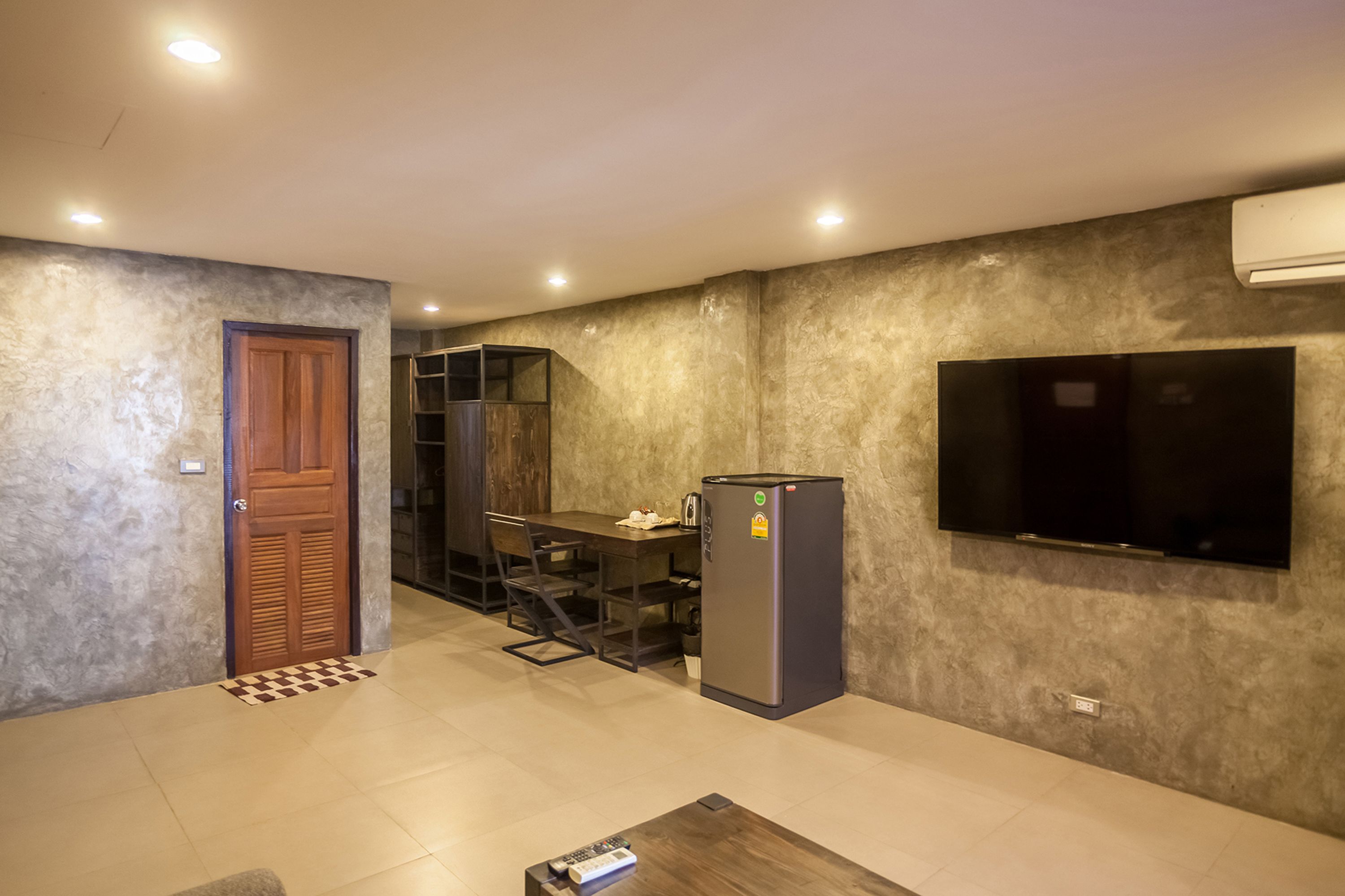 A compact living space with a kitchenette, a flat-screen TV mounted on the wall, and a wooden door.