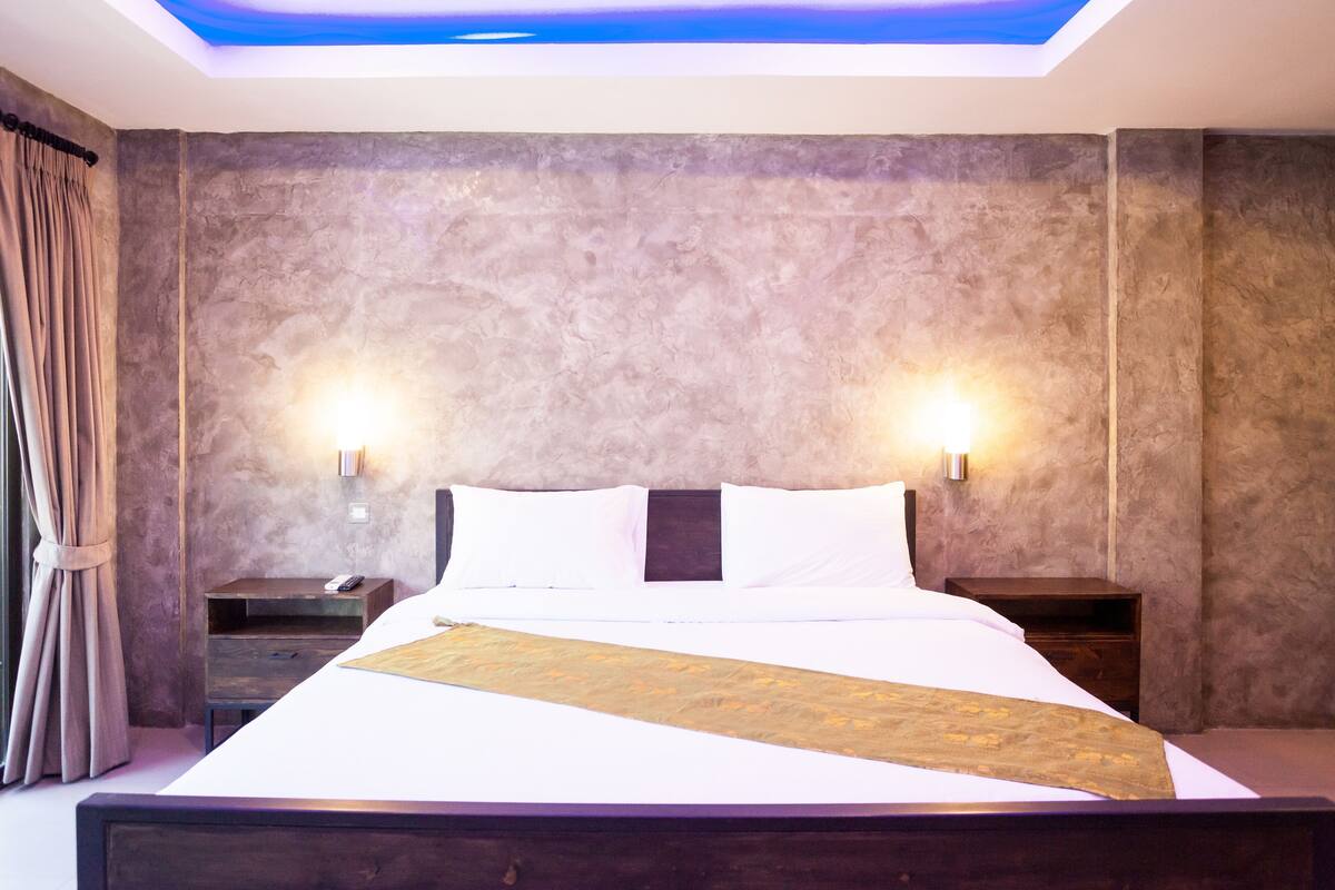 Une chambre moderne avec un grand lit, deux tables de chevet, un luminaire au plafond et une vue sur le ciel grâce à une lucarne.