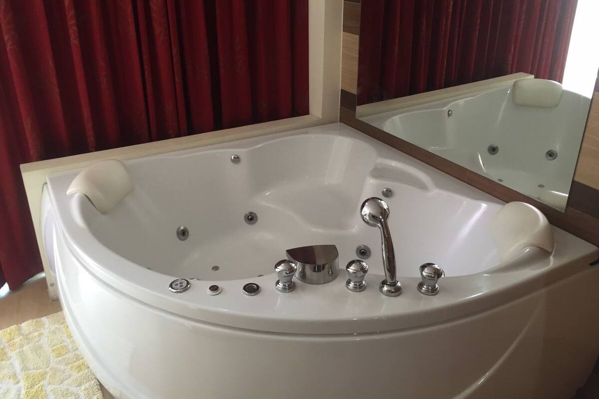 Une salle de bain moderne avec une grande baignoire, un miroir et des rideaux rouges.