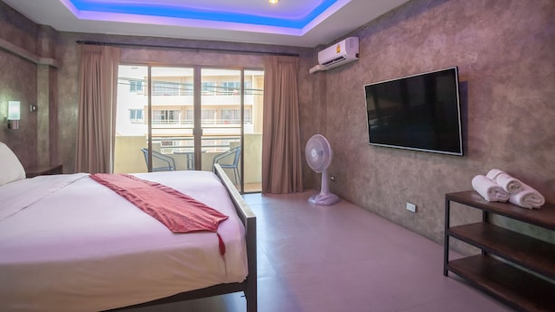 Hotelkamer met een bed, een aan de muur bevestigde televisie, een ventilator en een balkon met uitzicht op gebouwen.