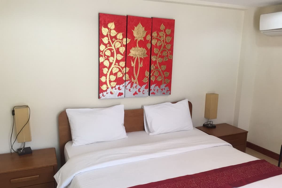 Une chambre d’hôtel comprenant un lit, deux tables de chevet, un climatiseur fixé au mur et un panneau décoratif rouge placé au-dessus du lit.
