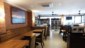 Een restaurant met houten tafels, comfortabele banken, een bakstenen muur en een groot schilderij.