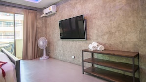 Hotelkamer met een grote flatscreen televisie aan de muur, een ventilator, een houten tv-meubel met handdoeken en een balkon met uitzicht.
