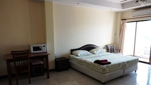 A bedroom with a bed, a desk with a microwave, a chair, and a nightstand. - Parinya's Apartment (Pattaya)
