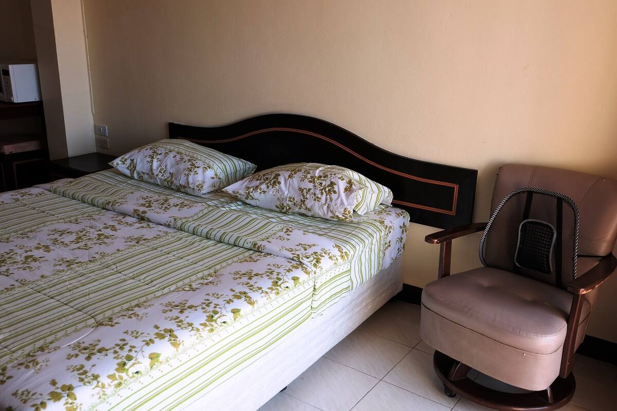 A neatly made bed with floral bedding, a wooden headboard, and a brown leather chair.